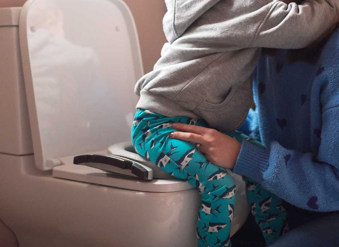 Parent helps toddler onto the toilet which has a Potette 2 in 1 on it